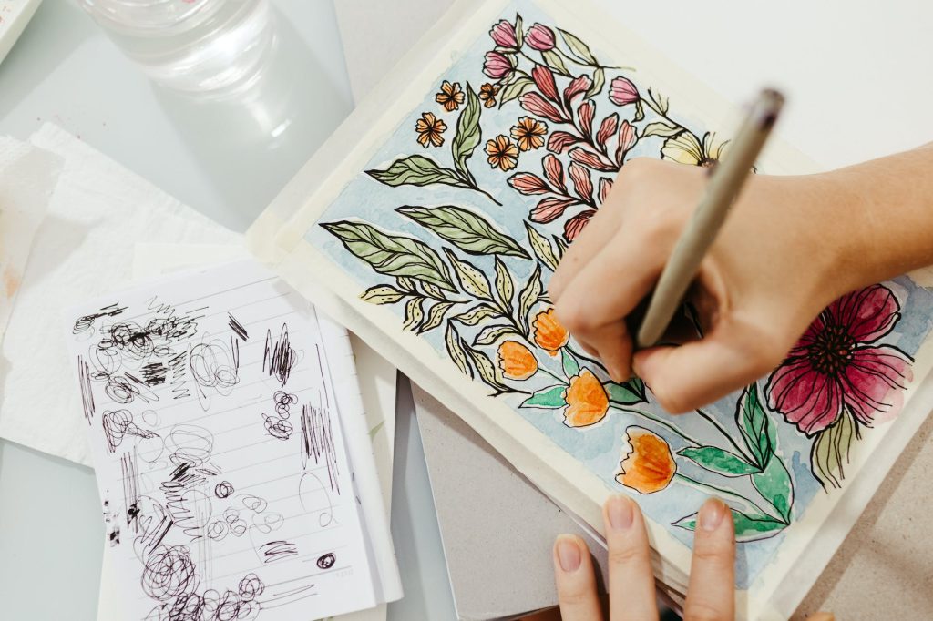 a person coloring a floral drawing on sketch pad